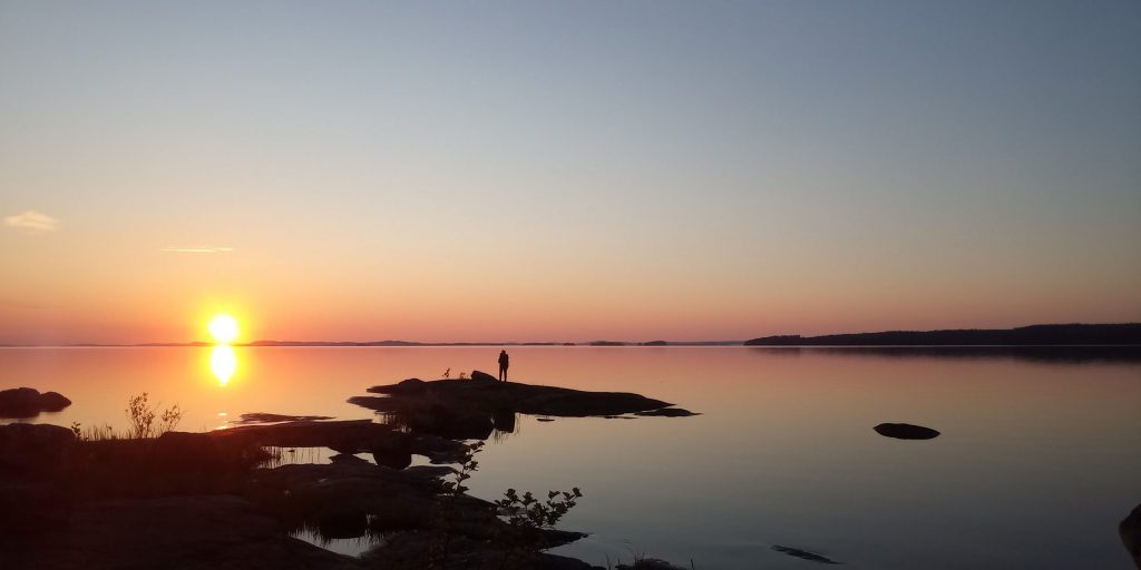 Hyvinvointiblogi. Kuvassa kaunis auringonlasku järven taakse. Etualalla kalliot.